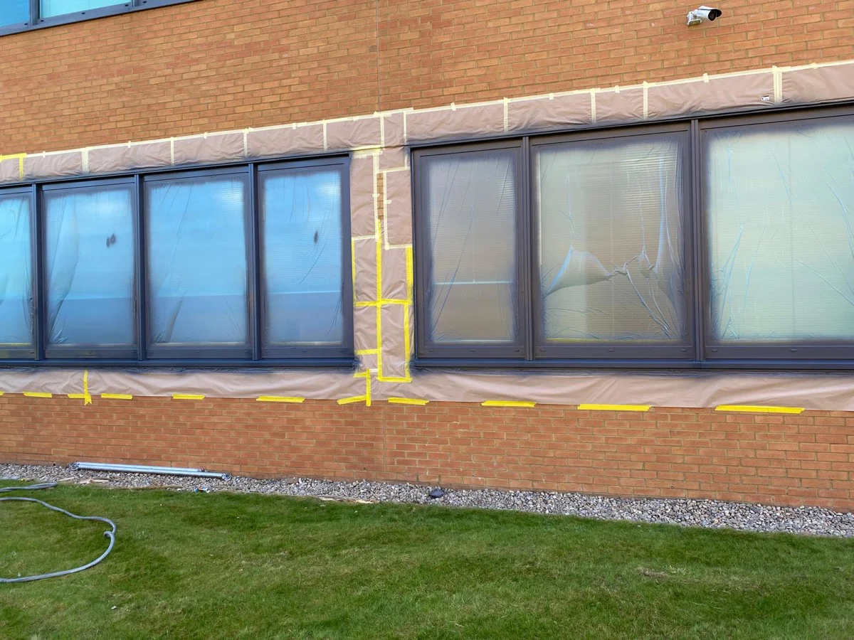 Ground floor curtain wall at Central Park Manchester fully masked with brown paper and tape ready for spraying