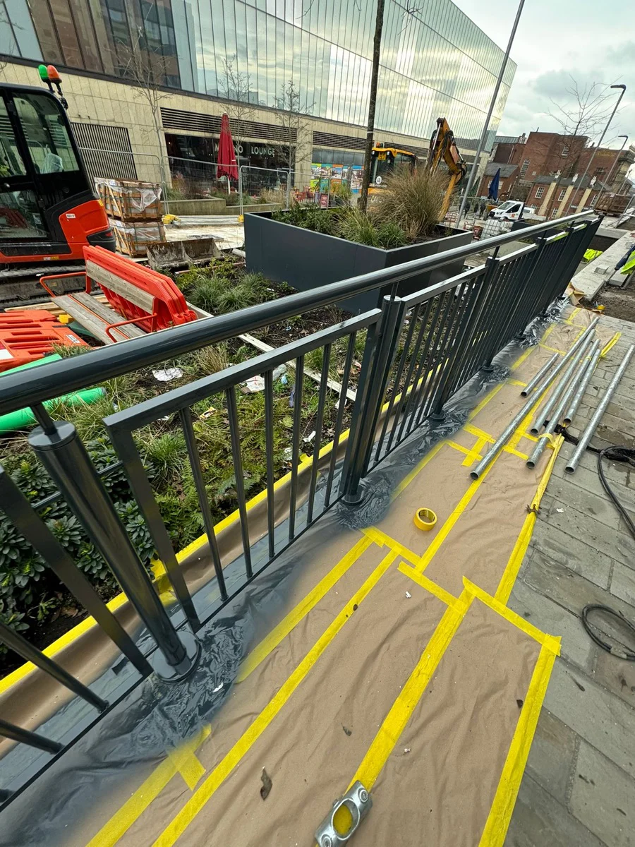 Wider view of balustrade run at Manchester city centre development during electrostatic spraying, city centre buildings in background