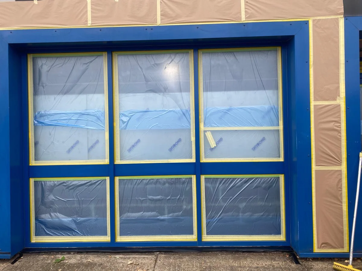 Close-up of Halfords Autocentre Strood window bay during masking, blue frames and taped glazing
